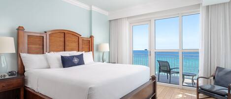 Un dormitorio de hotel con una cama grande, una mesita de noche, una silla y un balcón con vista al océano.