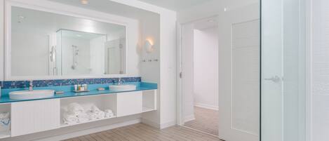 Un baño moderno con un espejo grande, dos lavamanos y una cabina de ducha de vidrio.