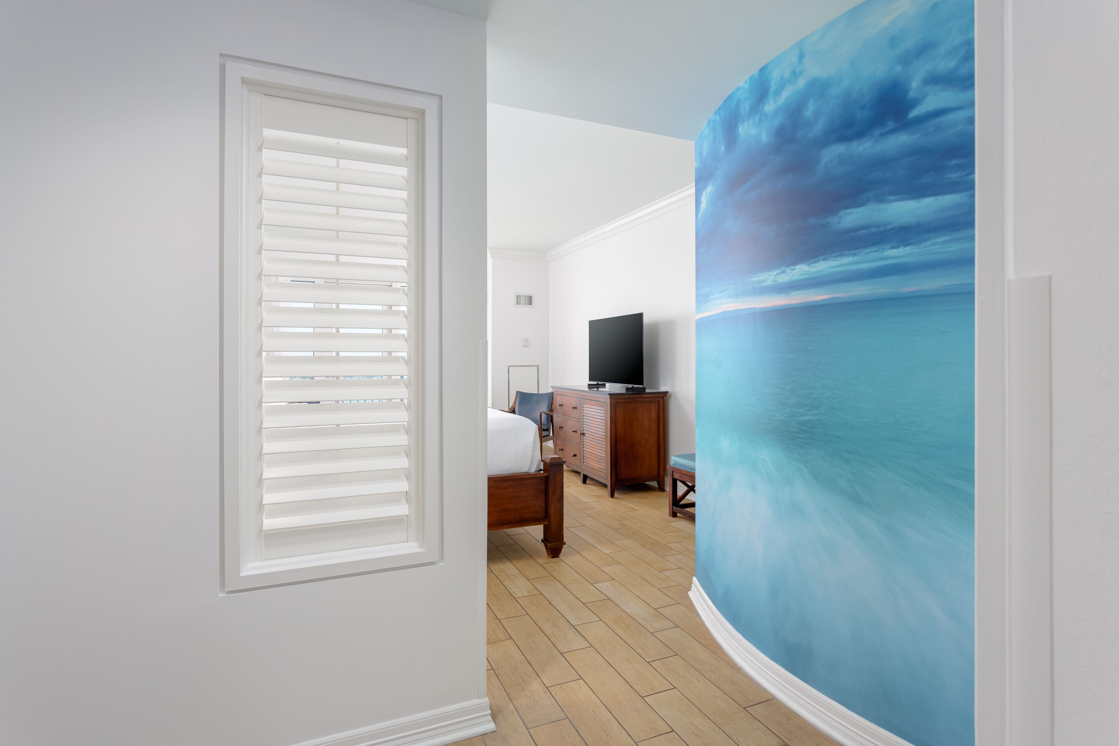 Een slaapkamer met een groot raam, een bed, een dressoir en een televisie.