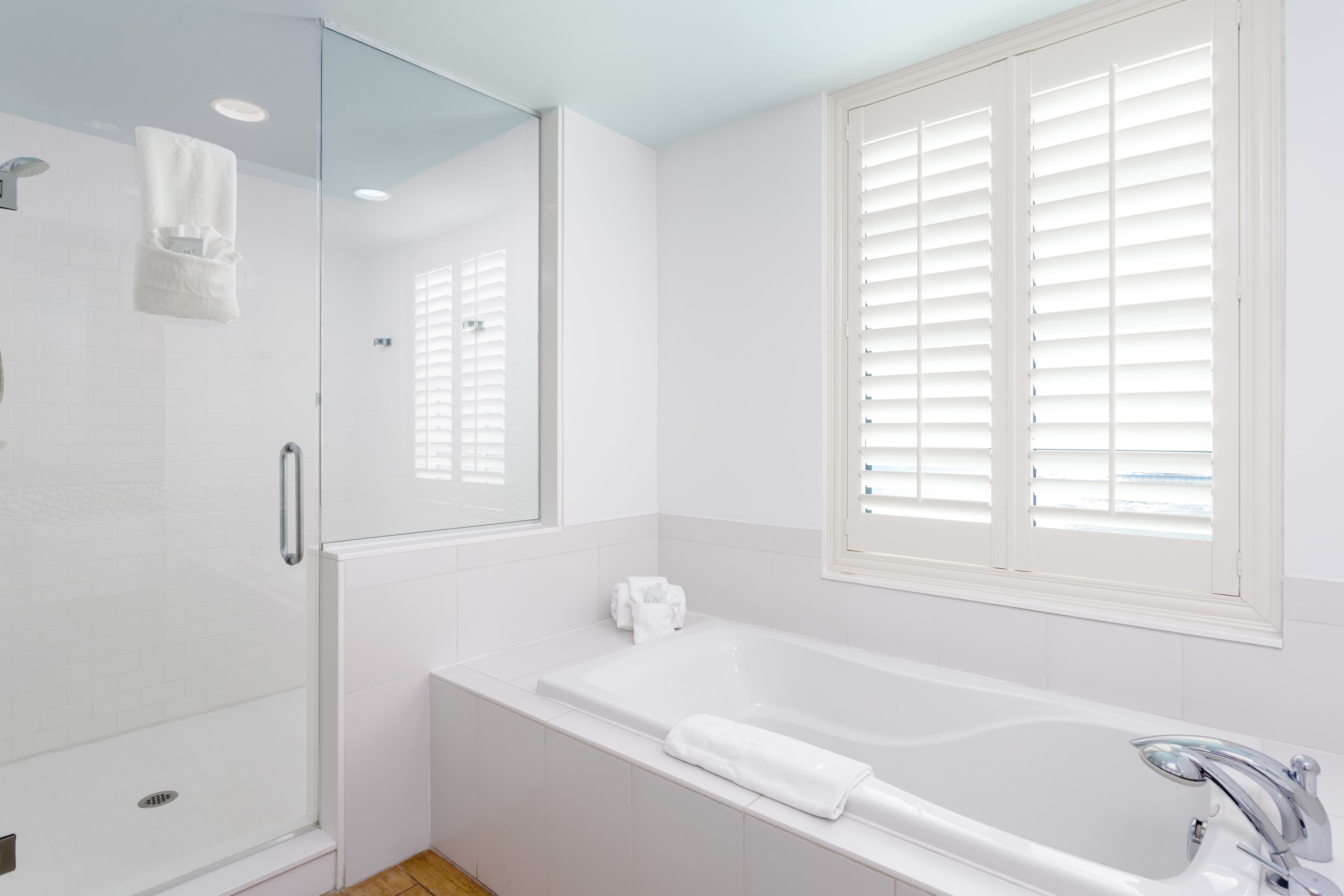 Un baño moderno con cabina de ducha de vidrio, una bañera grande y una ventana con persianas.