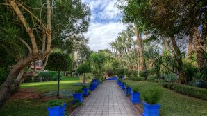 Un sendero pavimentado bordeado de macetas azules y diversos árboles, que atraviesa un jardín cuidado.