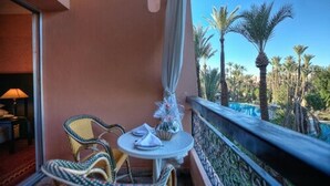 Un balcón con sillas de mimbre y una mesa, con vistas a un jardín con palmeras.