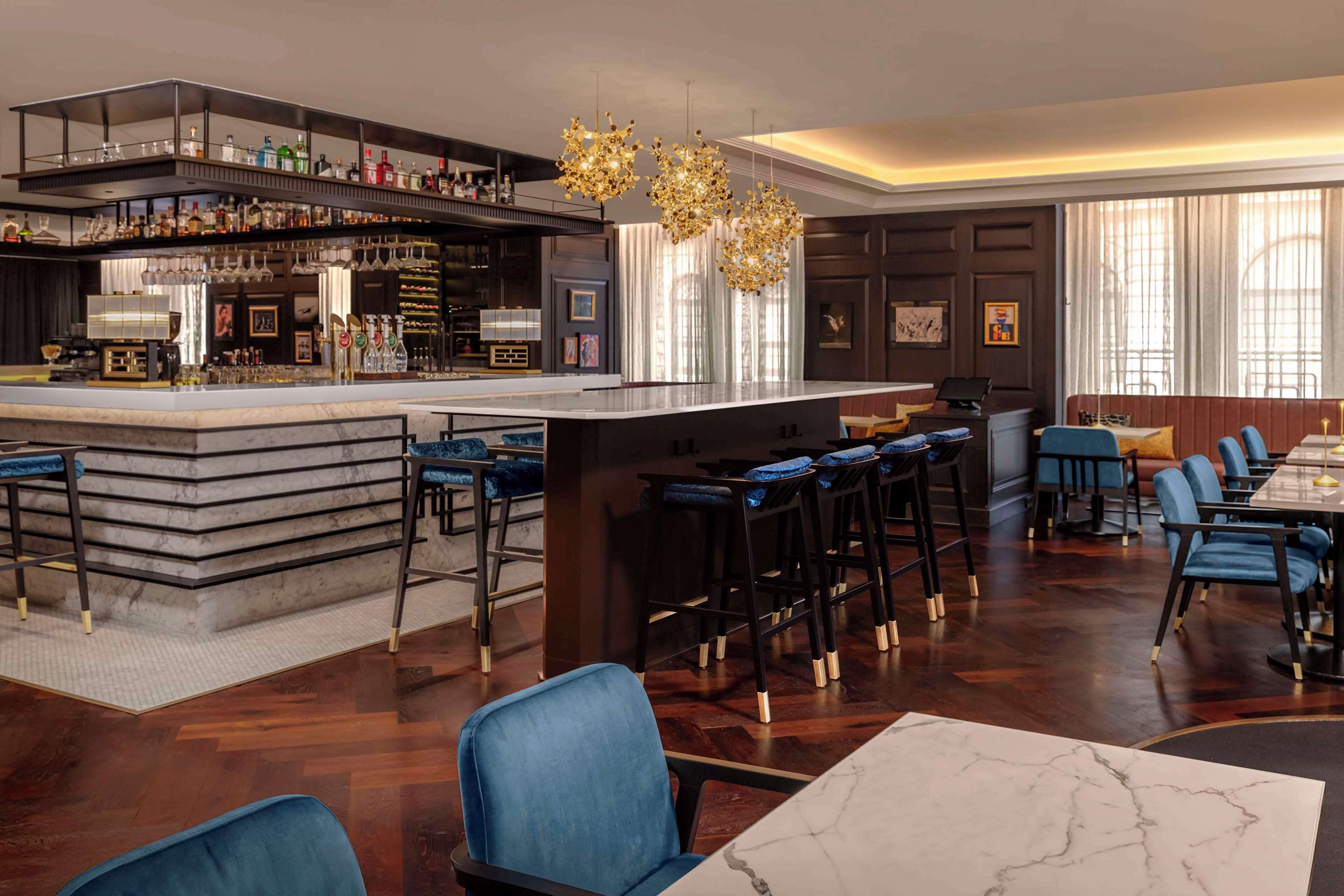 A modern bar area with a marble countertop, bar stools, and a variety of bottles and glasses.
