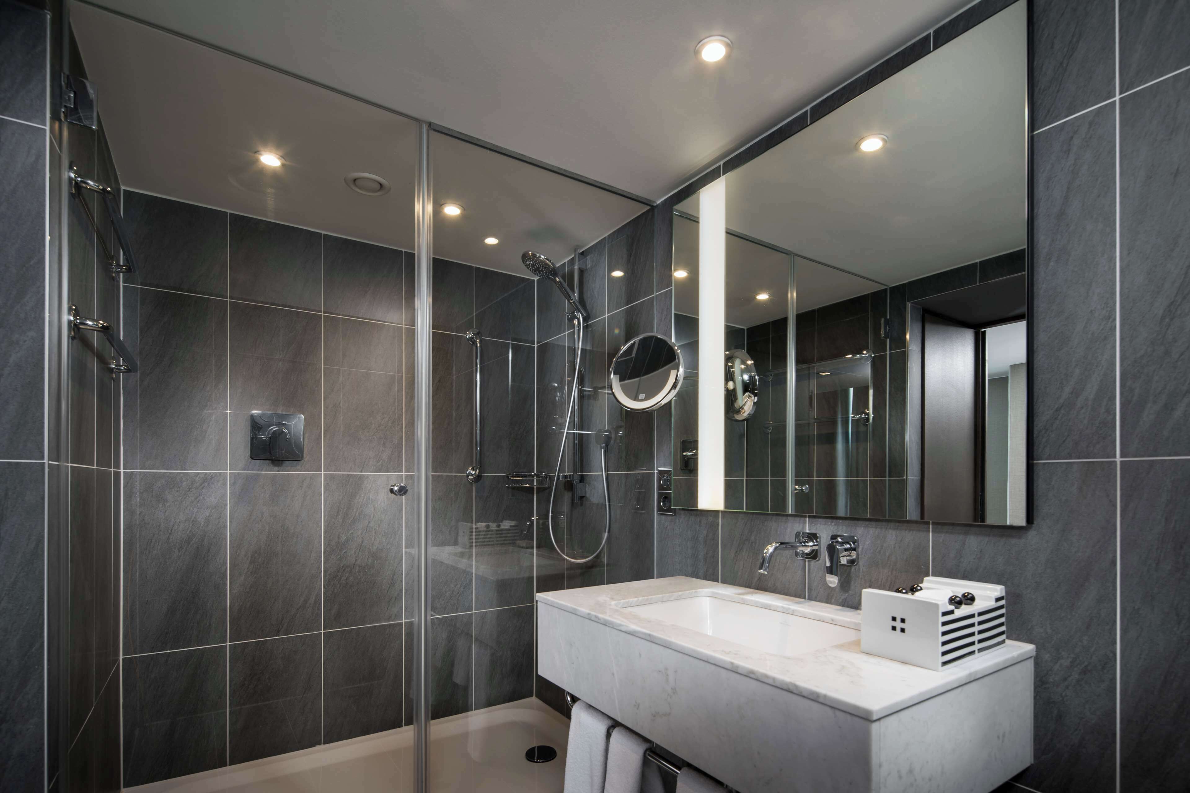 Un baño moderno con ducha de vidrio, un espejo grande y un lavamanos blanco.
