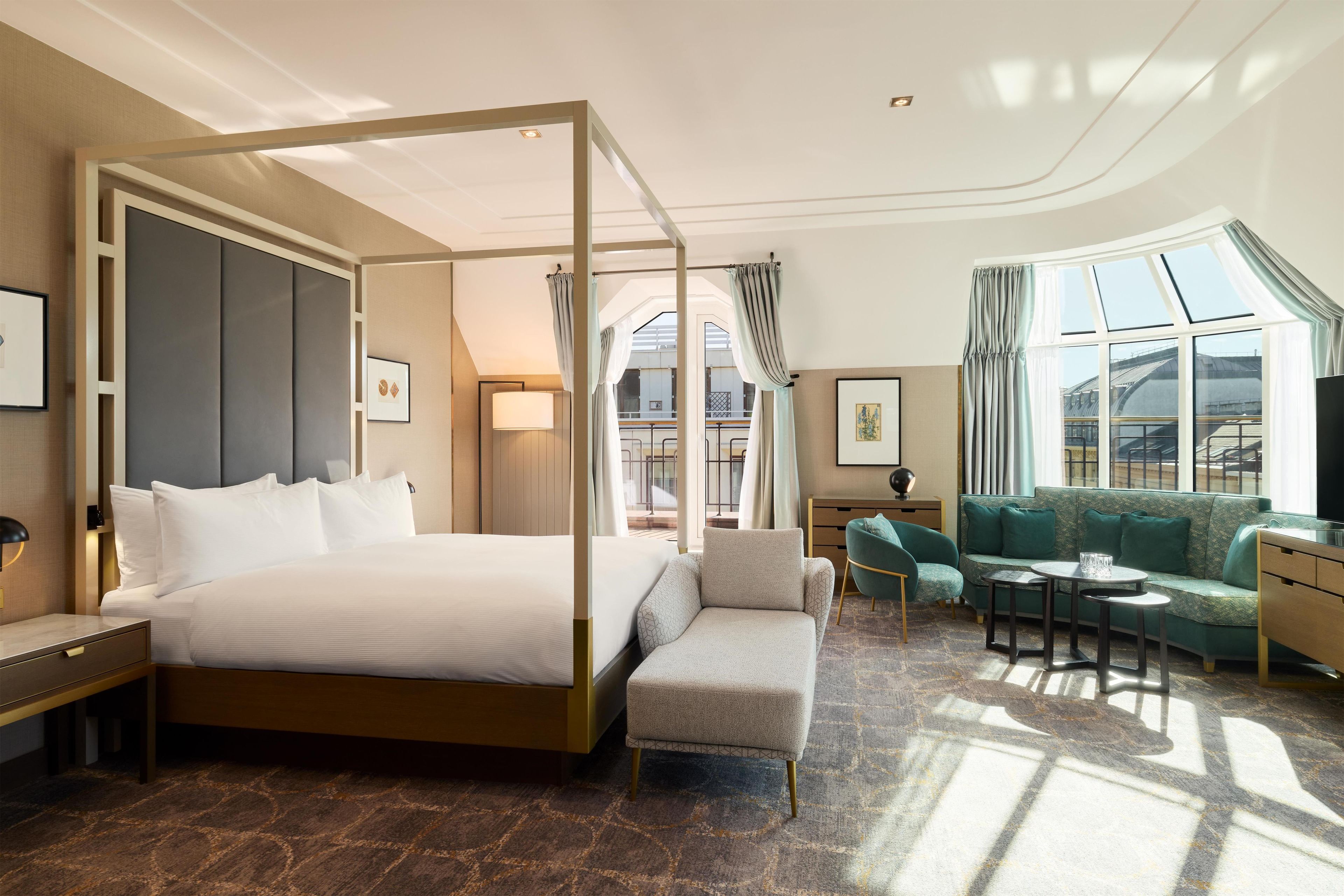 A hotel room with a four-poster bed, a sofa, a small table, and a window with curtains.