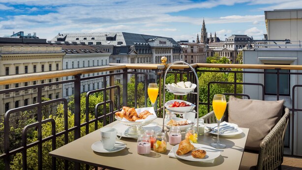 A balcony with a breakfast setup including croissants, fruit, and juice, overlooking a cityscape with historic buildings. - Hilton Vienna Plaza (Vienna)