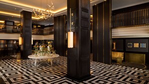 A lobby with a geometric patterned floor, a central round table with flowers, and a modern chandelier. - Hilton Vienna Plaza (Vienna)