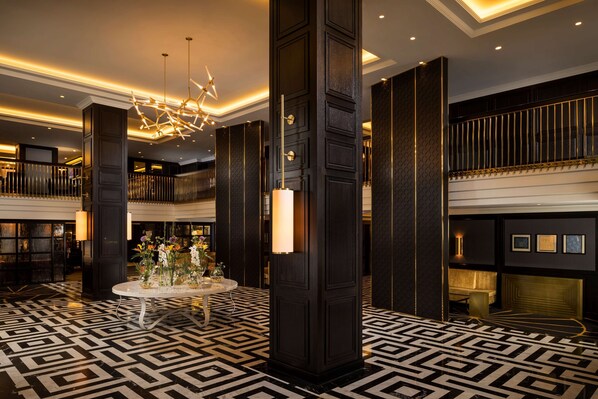Eine Lobby mit einem geometrisch gemusterten Boden, einem runden Tisch in der Mitte mit Blumen und einer modernen Kronleuchter.