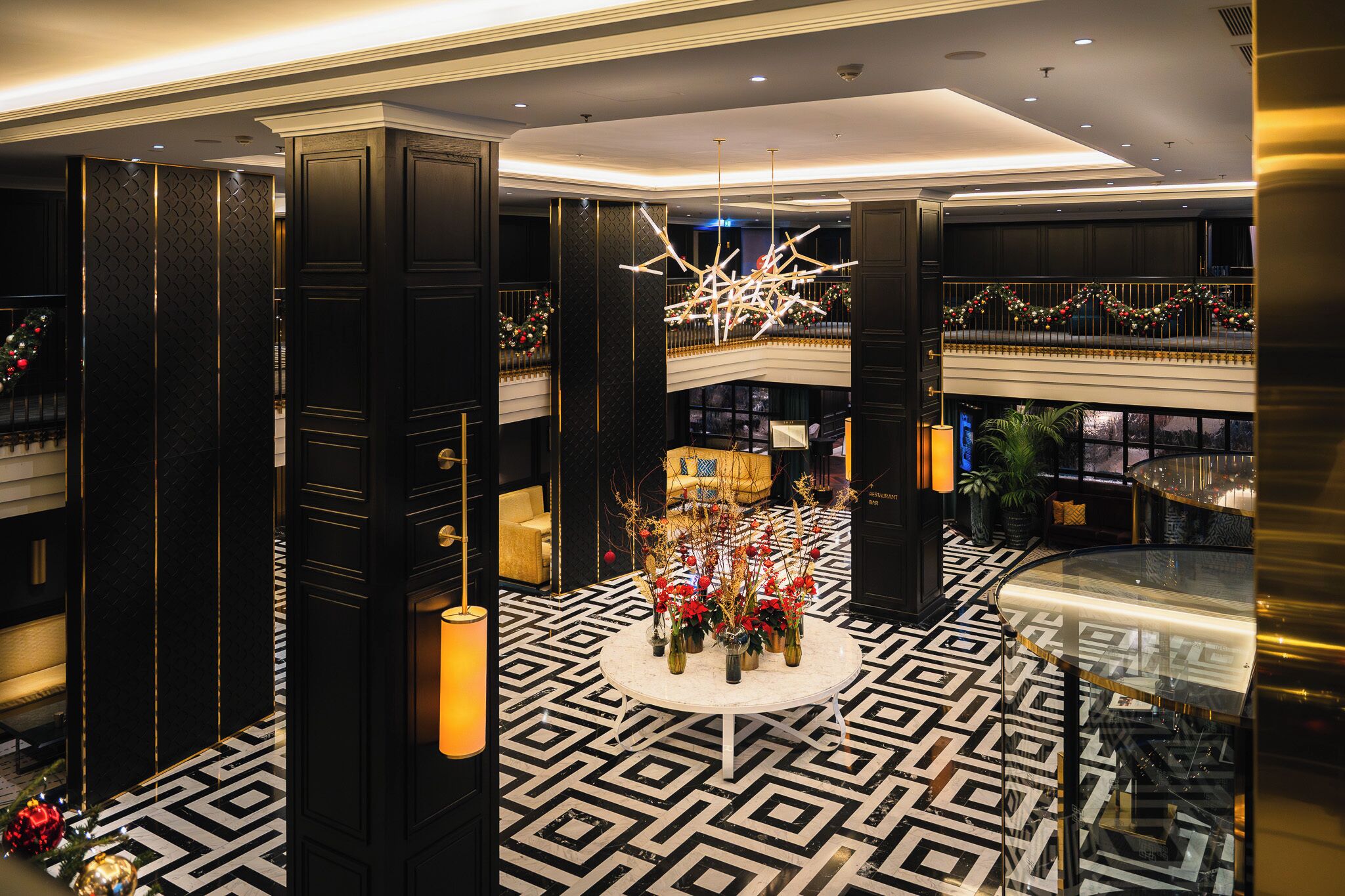 A lobby with a geometric patterned floor, a central round table with floral arrangements, and a modern chandelier.