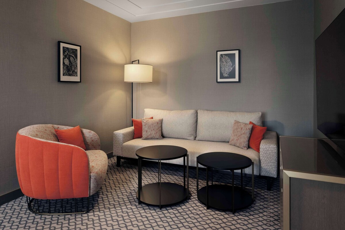 Una sala de estar moderna con un sofá, un sillón rojo, dos mesitas y dos cuadros enmarcados en las paredes.