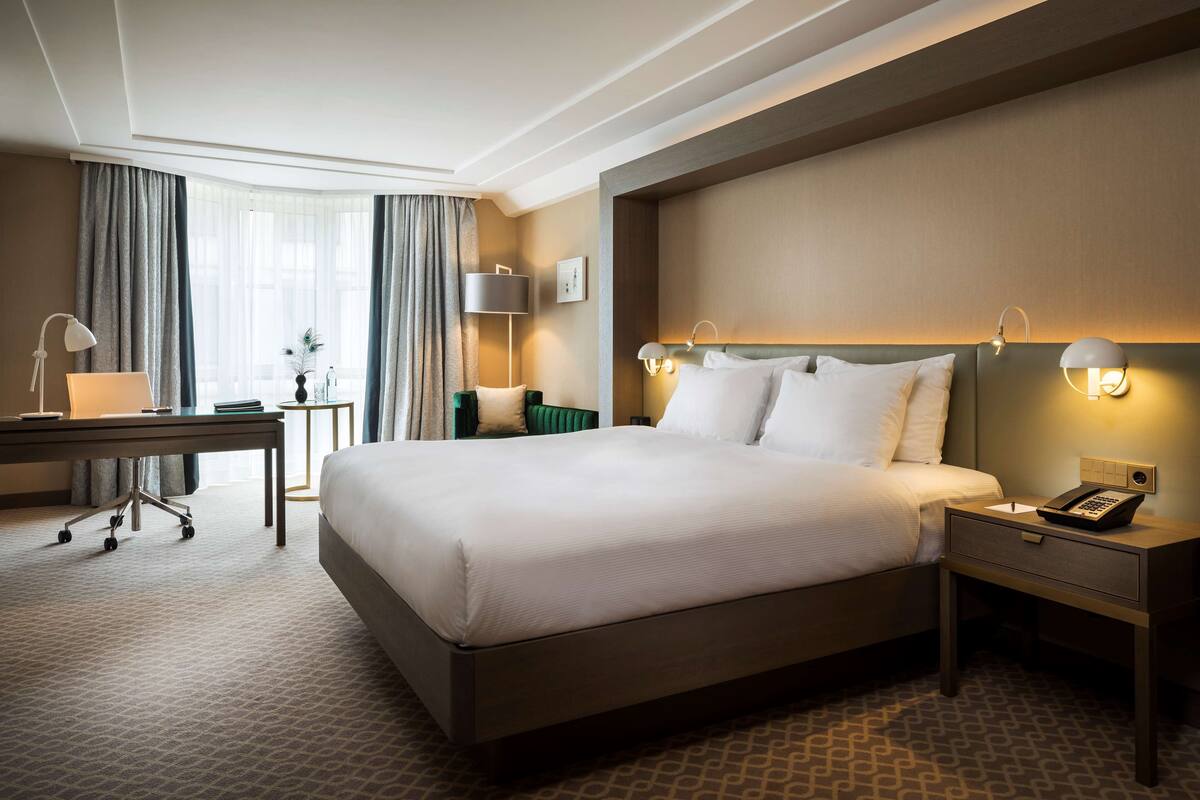 A hotel room with a large bed, bedside tables, a desk, and a lamp.