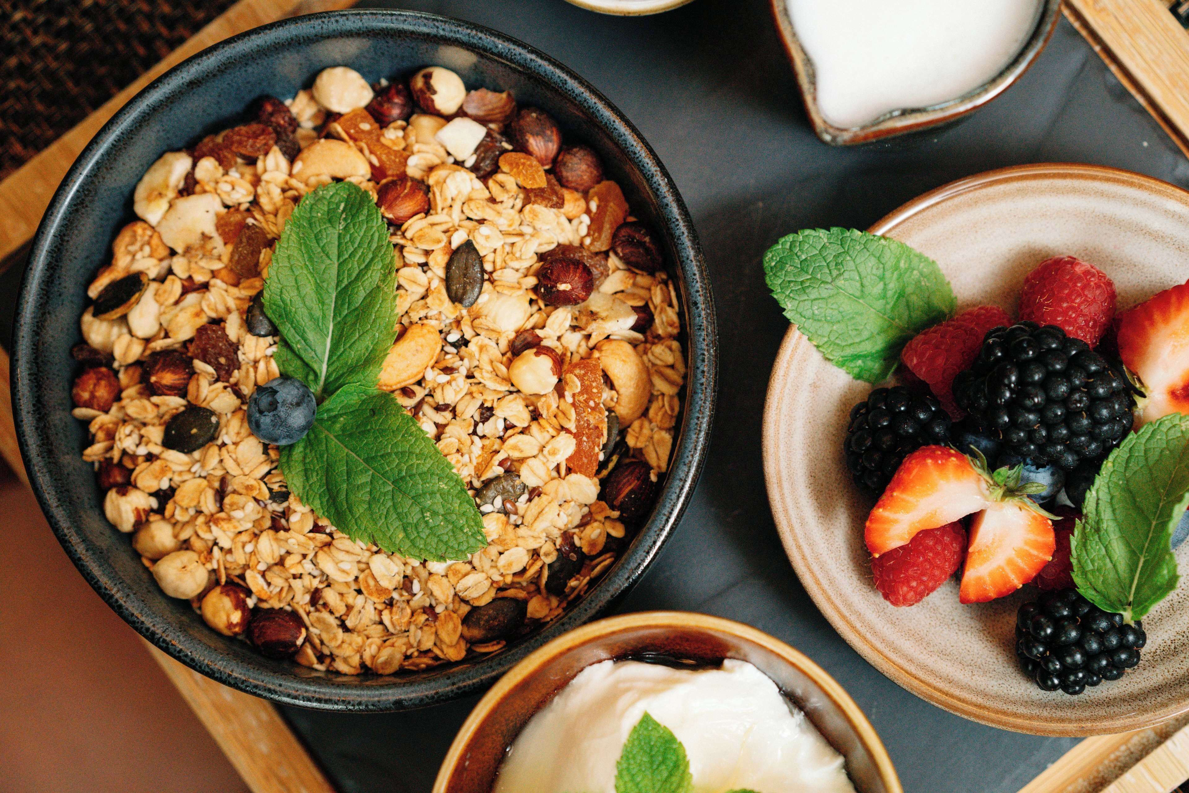 A bowl of granola with nuts and dried fruits, a bowl of mixed berries, and a small bowl of yogurt.