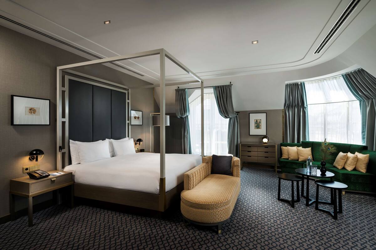 A hotel room with a four-poster bed, a sofa, a small table, and a chair.