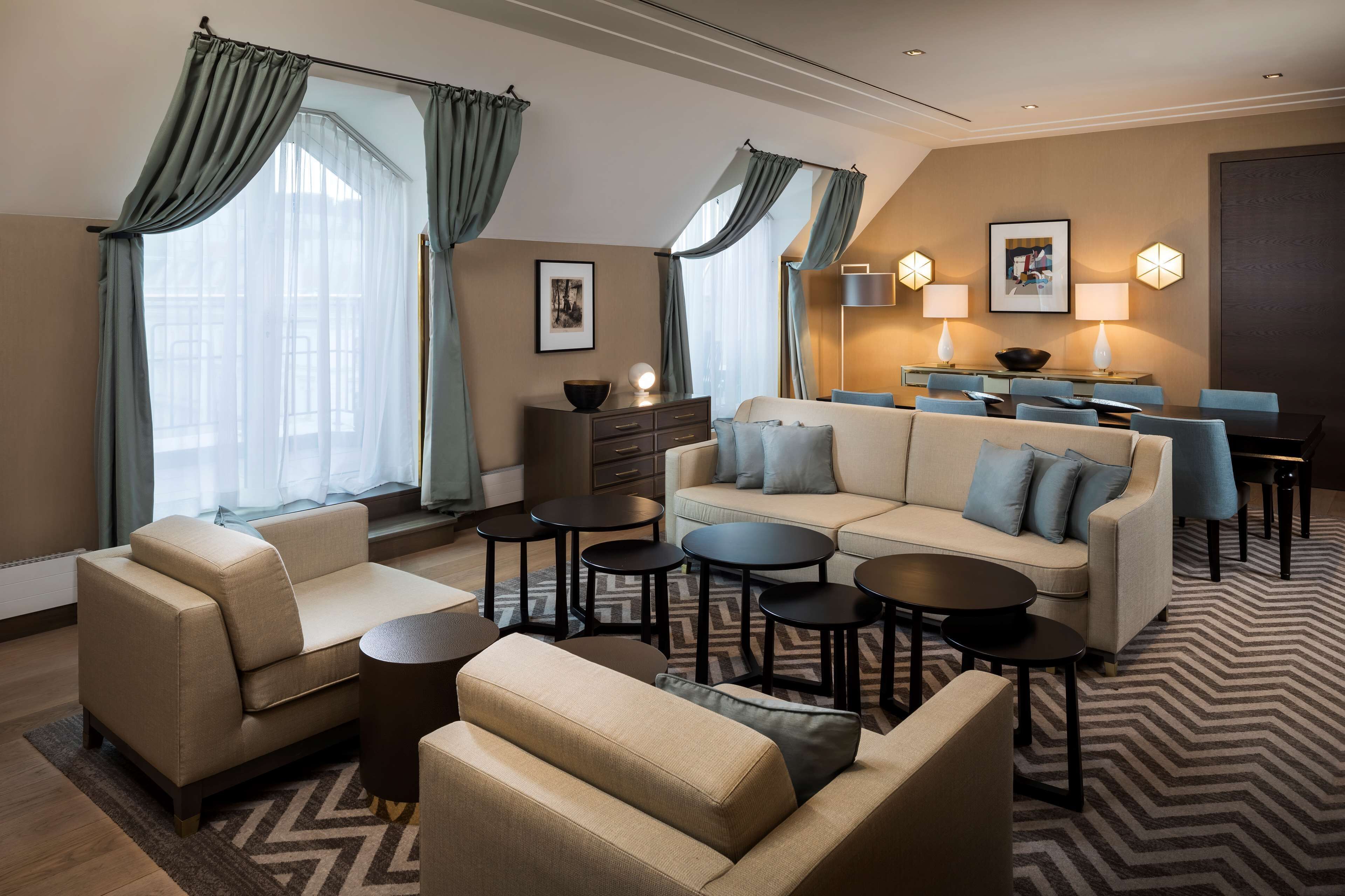 Una habitación de hotel moderna con sofá, sillones, una mesa de comedor y una mesita de centro.