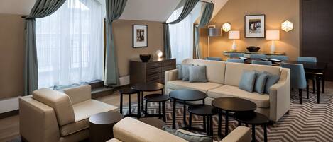 Una habitación de hotel moderna con sofá, sillones, una mesa de comedor y una mesita de centro.