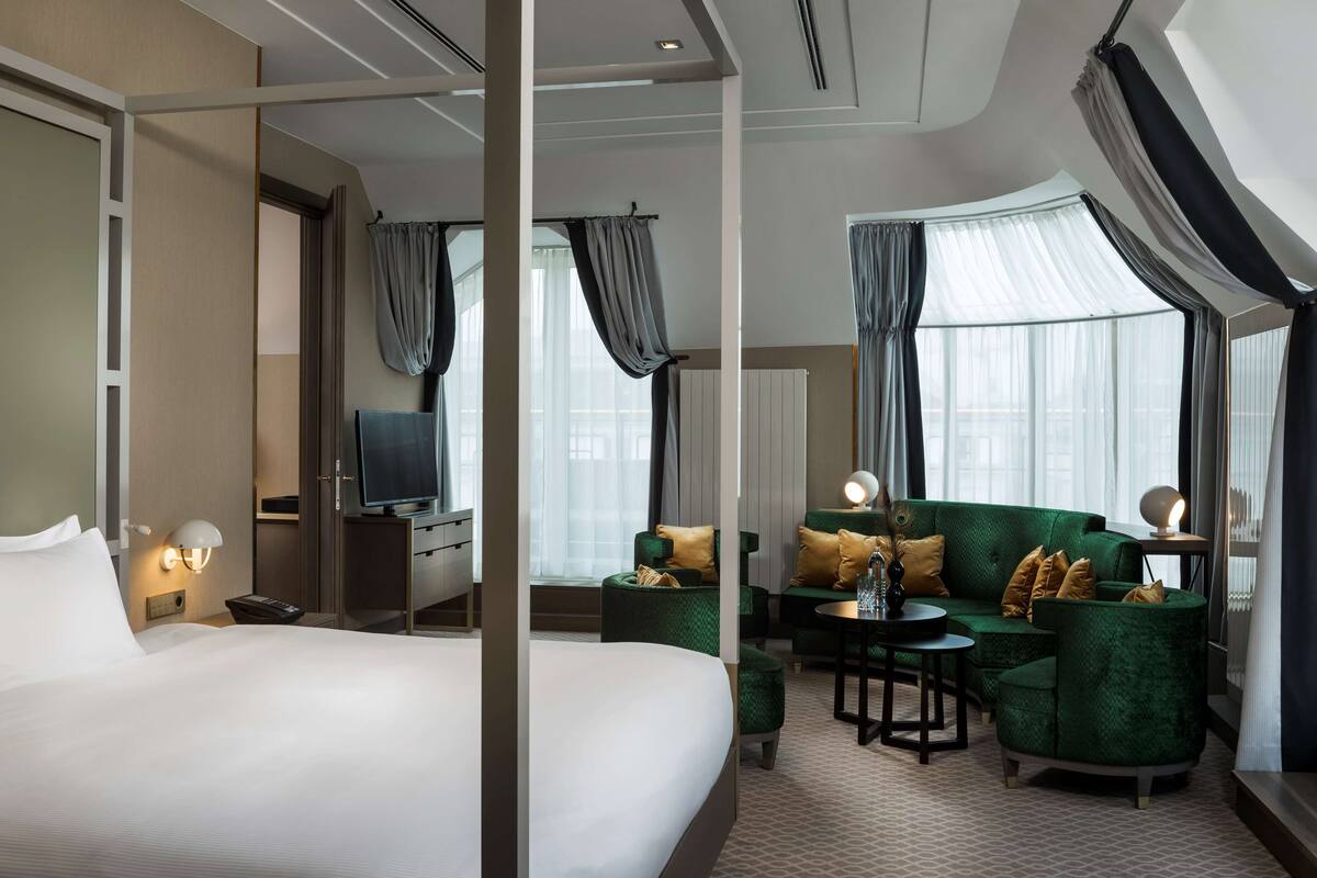 A hotel room with a large bed, a TV, a sofa set, and a small table.