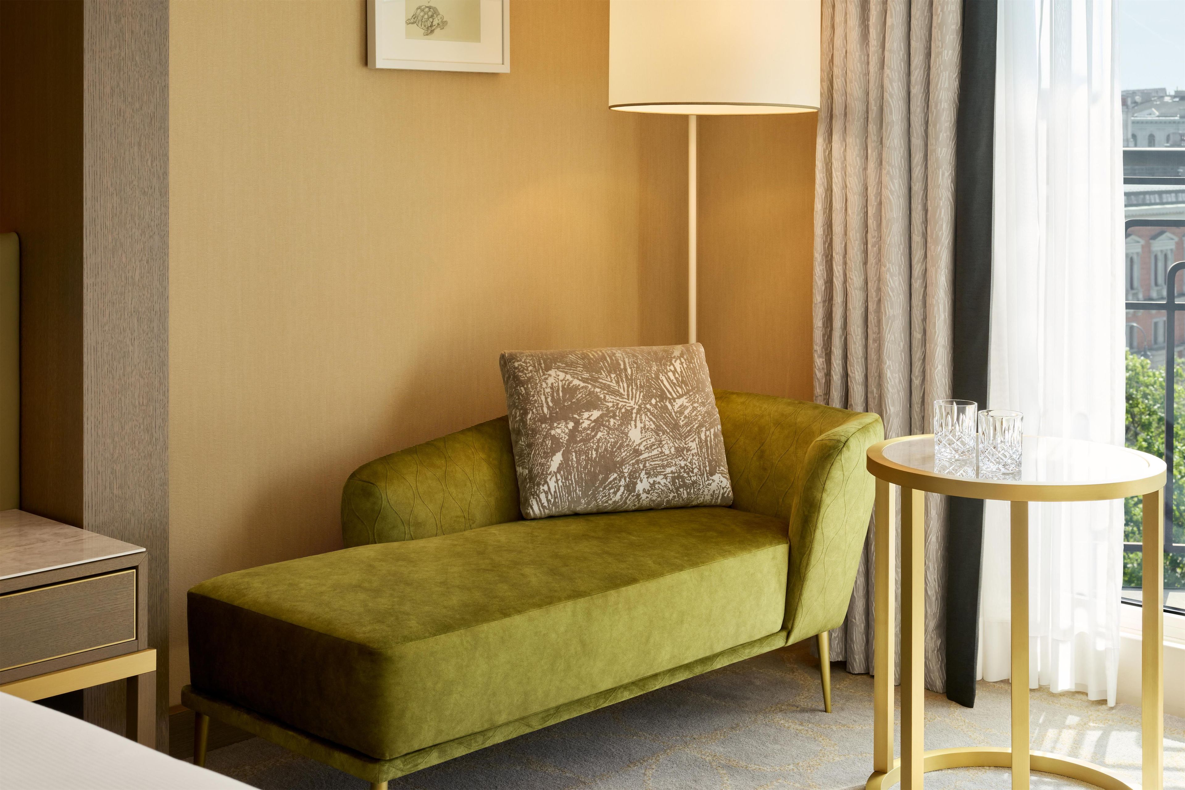 A green sofa with a patterned pillow, a small round table with glasses, and a lamp.