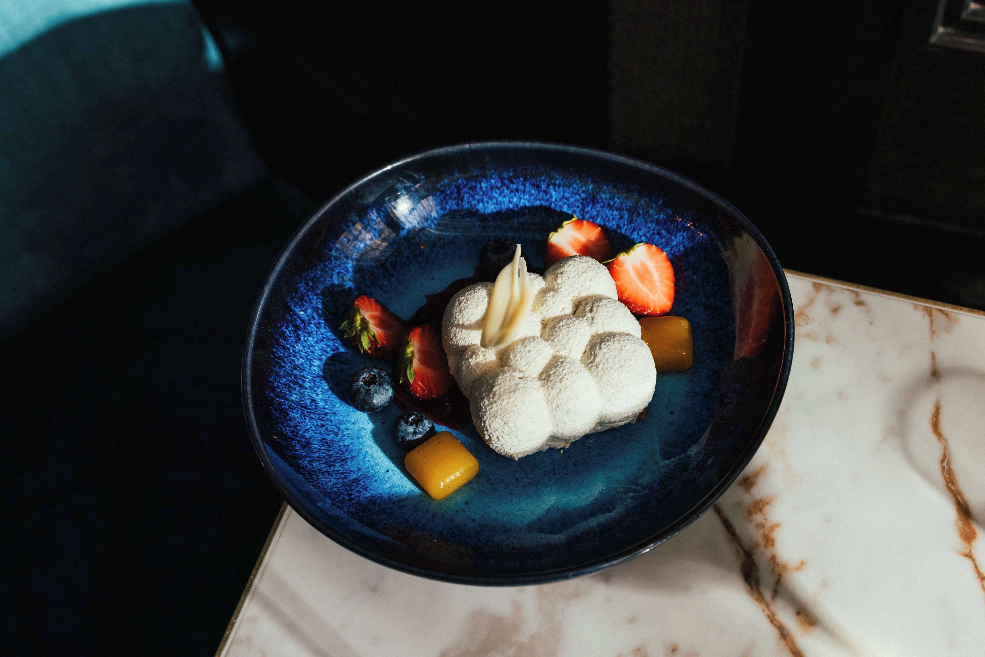 A dessert on a blue plate with strawberries, blueberries, and a dollop of cream.