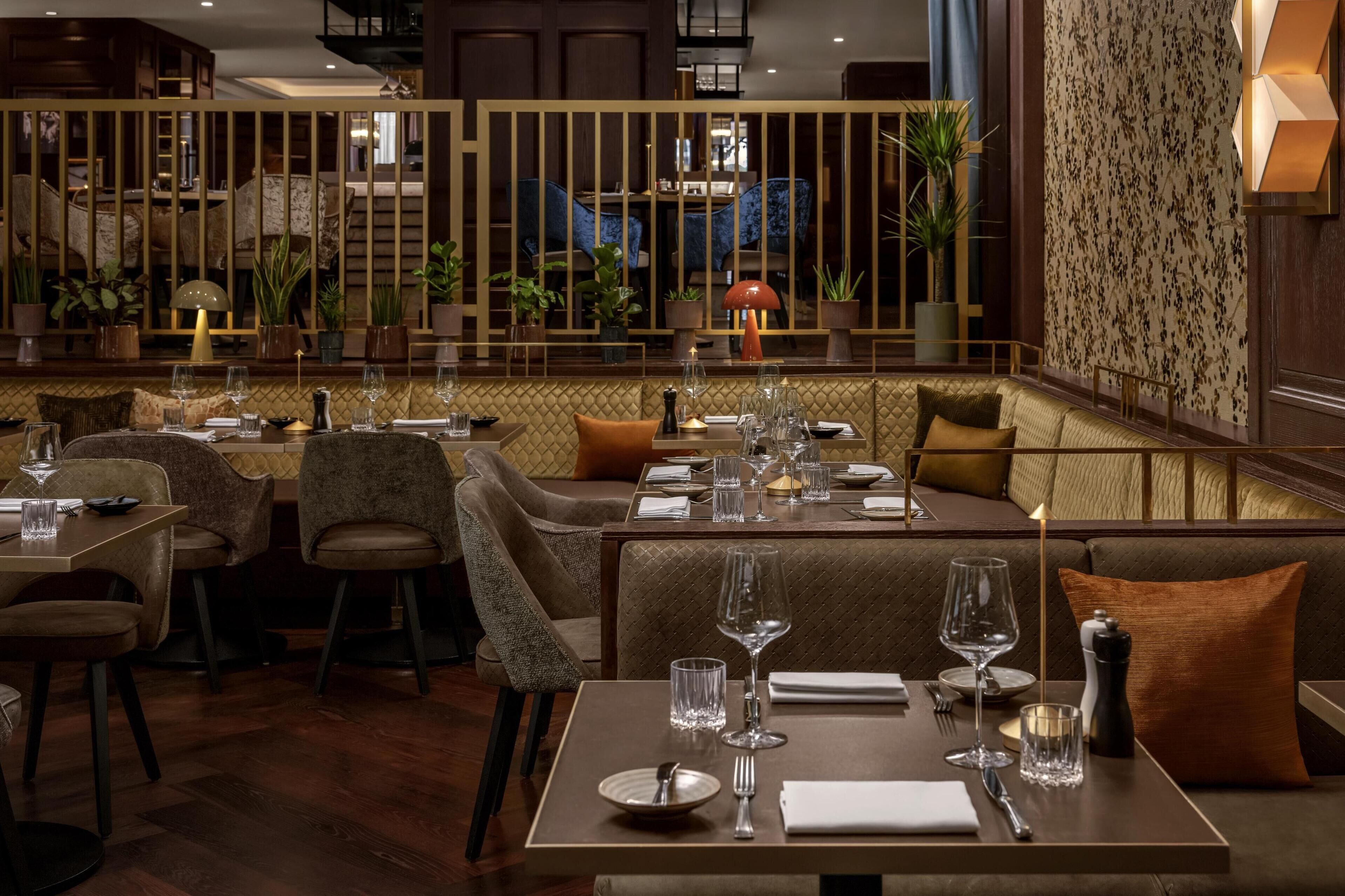 Un ristorante dall'atmosfera accogliente, caratterizzato da pannelli in legno, sedute imbottite e vista su una sedia blu attraverso un divisorio decorativo.