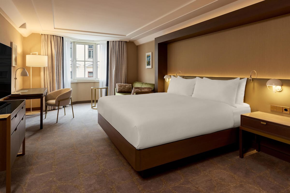 A hotel room with a large bed, a desk with a chair, a TV, and a window with curtains.
