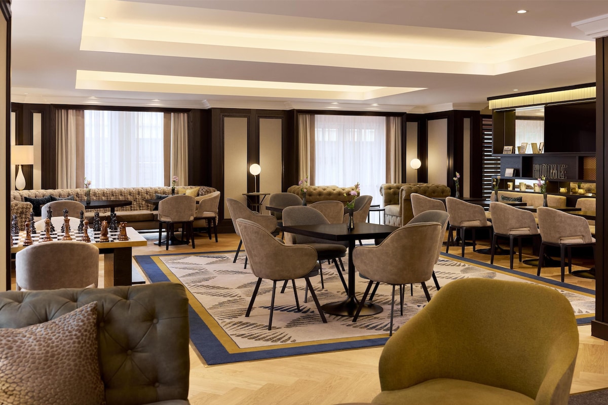 Un amplio hall de hotel con una gran zona de estar, una mesa de ajedrez y un ambiente luminoso.