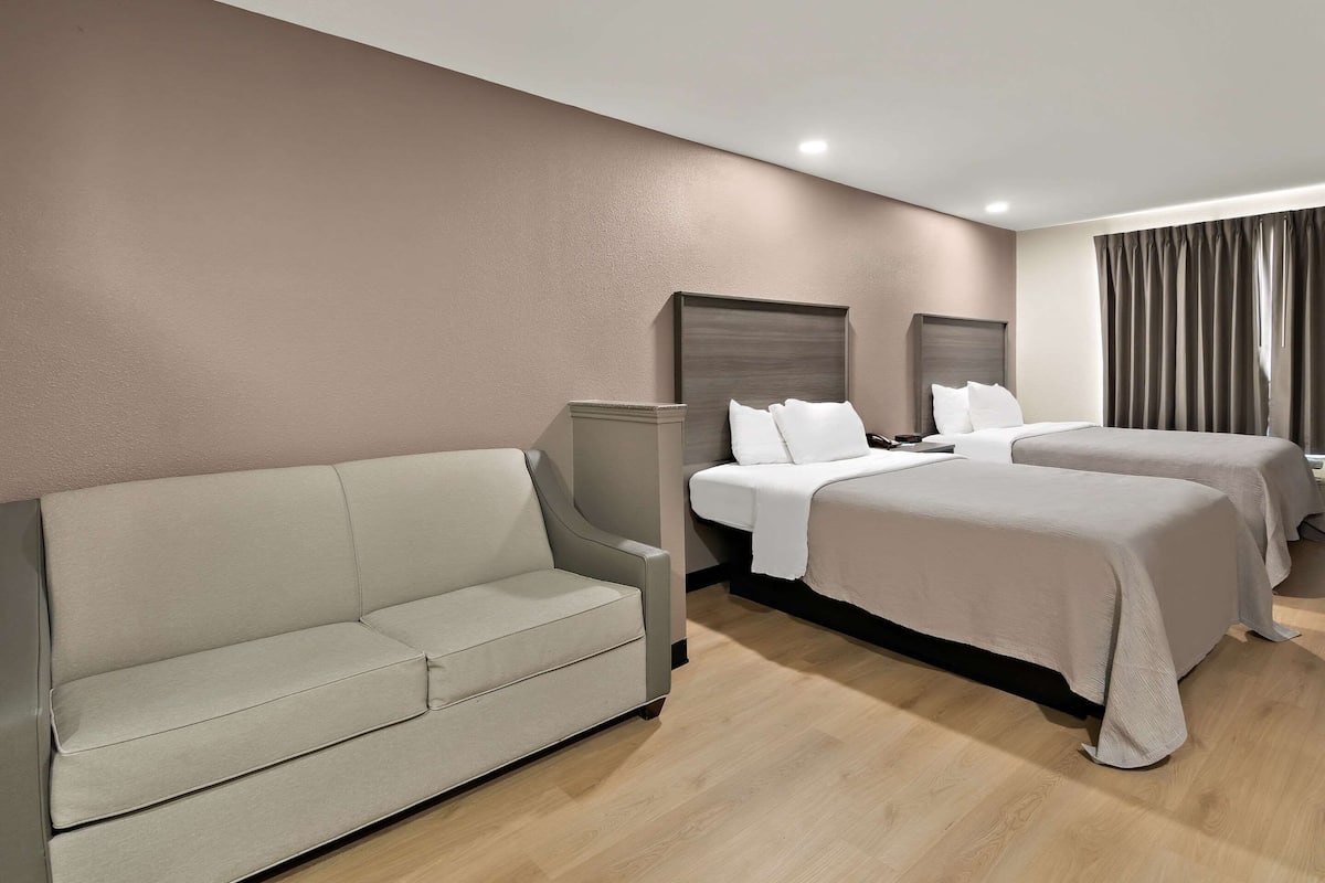 A hotel room with a sofa, two beds, and a large window with curtains.