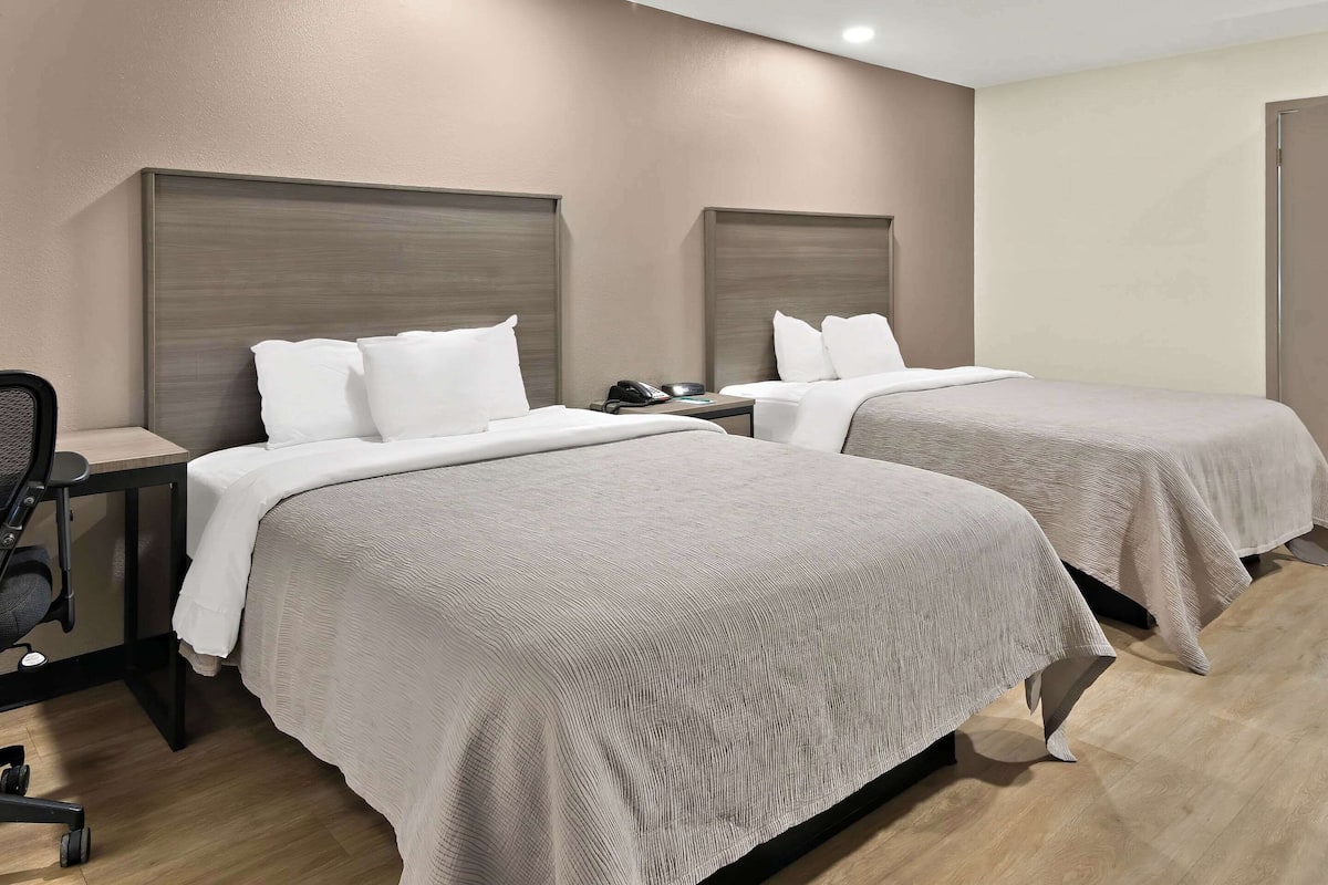 A hotel room with two beds, a desk, and a chair.