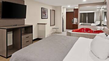 A hotel room with a bed, a TV mounted on a wooden cabinet, a red bathtub, and a large mirror.