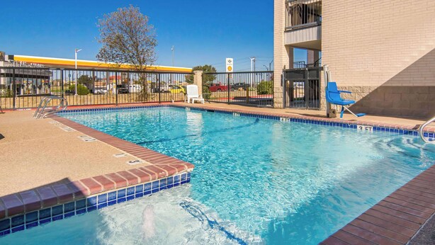 A swimming pool with a tiled edge, a brick deck, and a metal fence.
