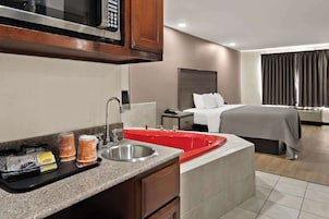 Habitación de hotel con kitchenette, cama, baño y un amplio ventanal con cortinas.