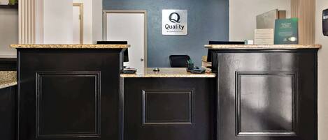 A reception area with two black reception desks, a blue wall with a 'Quality by Choice Hotels' sign, and a 'Credit Card Advice' sign.