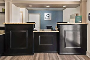 Zona de recepción con dos mostradores negros, una pared azul con un letrero de 'Quality by Choice Hotels' y un cartel de 'Asesoramiento con Tarjeta de Crédito'.