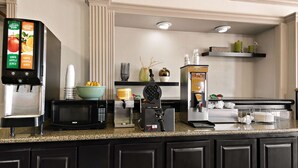 A kitchen area with a coffee machine, microwave, and juice dispenser.