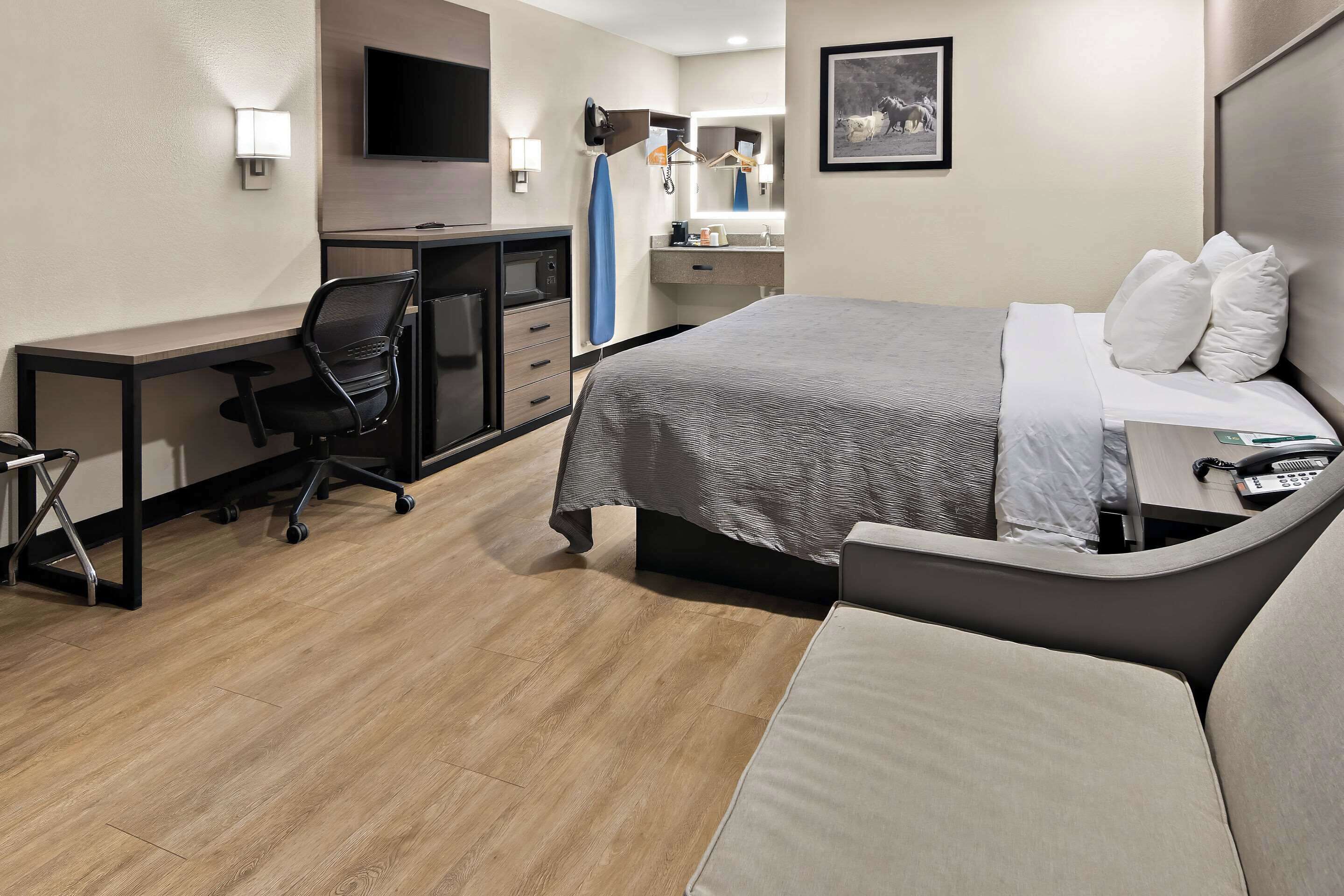 A hotel room with a bed, a desk, a chair, a TV, a mirror, and a bathroom.