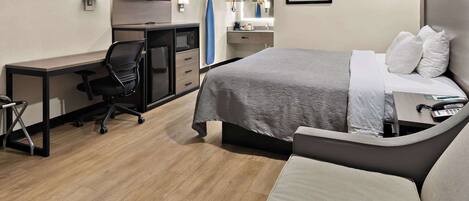 A hotel room with a bed, a desk, a chair, a TV, a mirror, and a bathroom.