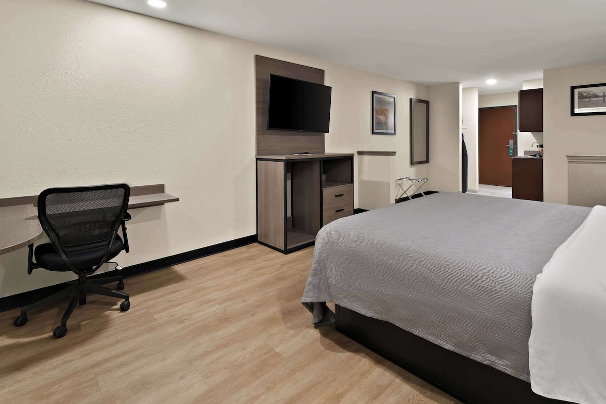 A hotel room with a bed, a desk with a chair, a TV mounted on the wall, and a door leading to a bathroom.