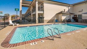 A swimming pool with a brick edge and a clear blue water surface, surrounded by a building with a brick facade and a covered patio area.