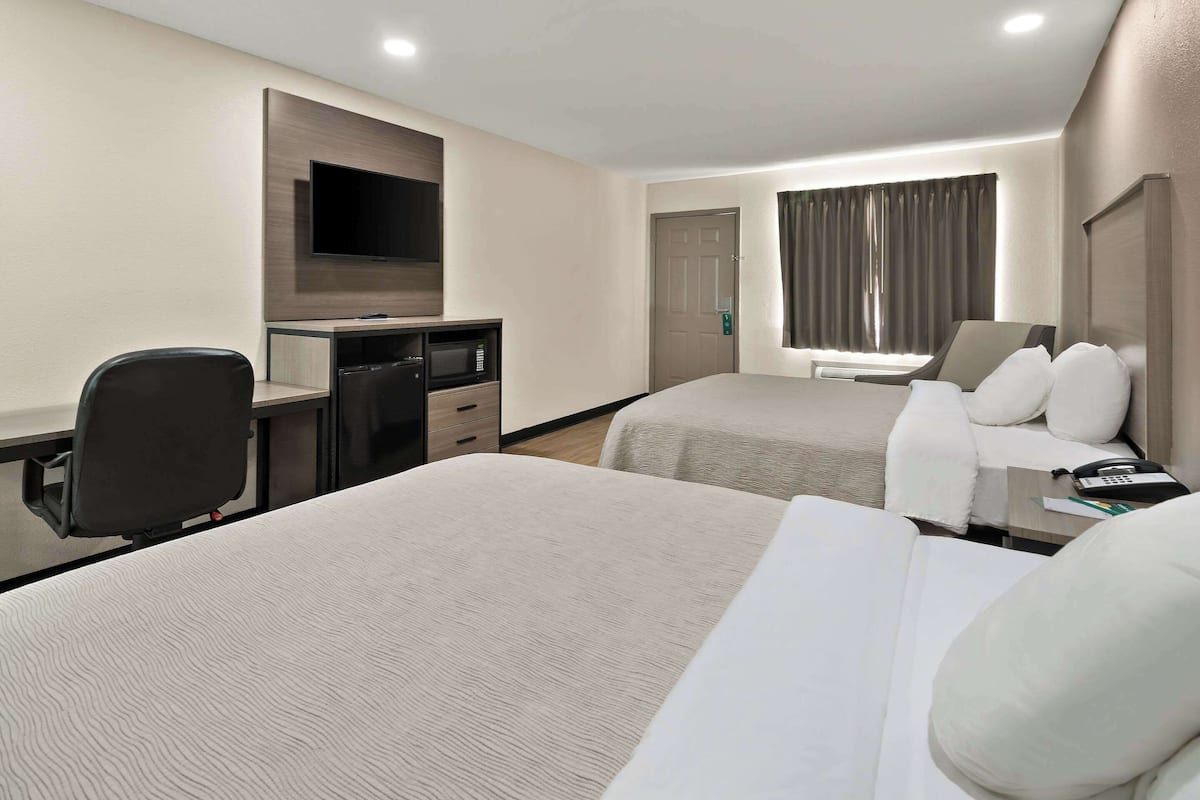 A hotel room with two beds, a desk with a TV, a microwave, and a telephone.
