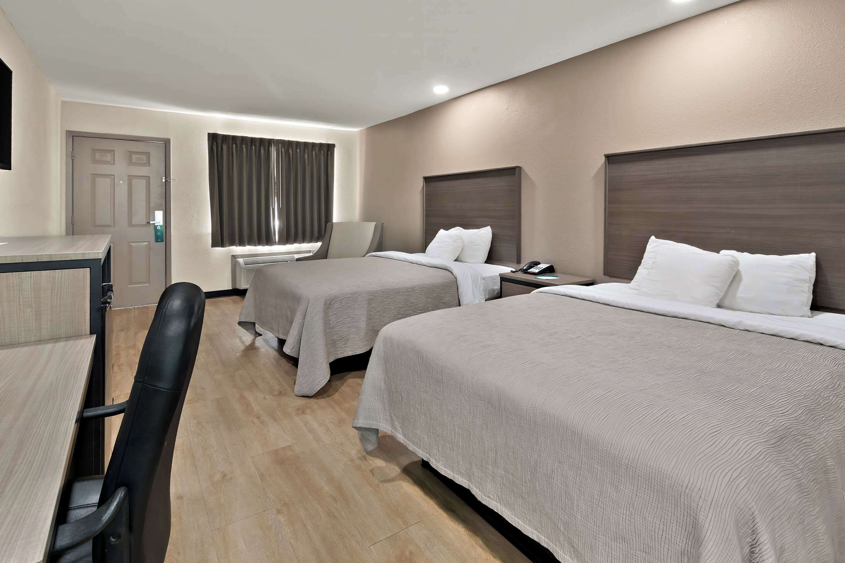 Hotellihuone, jossa on kaksi sänkyä, työpöytä ja tuoli.