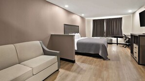 A hotel room with a bed, a sofa, a desk, and a TV.