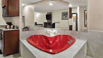 A modern bathroom with a heart-shaped red bathtub, a large mirror, and a vanity with a sink and towel rack.