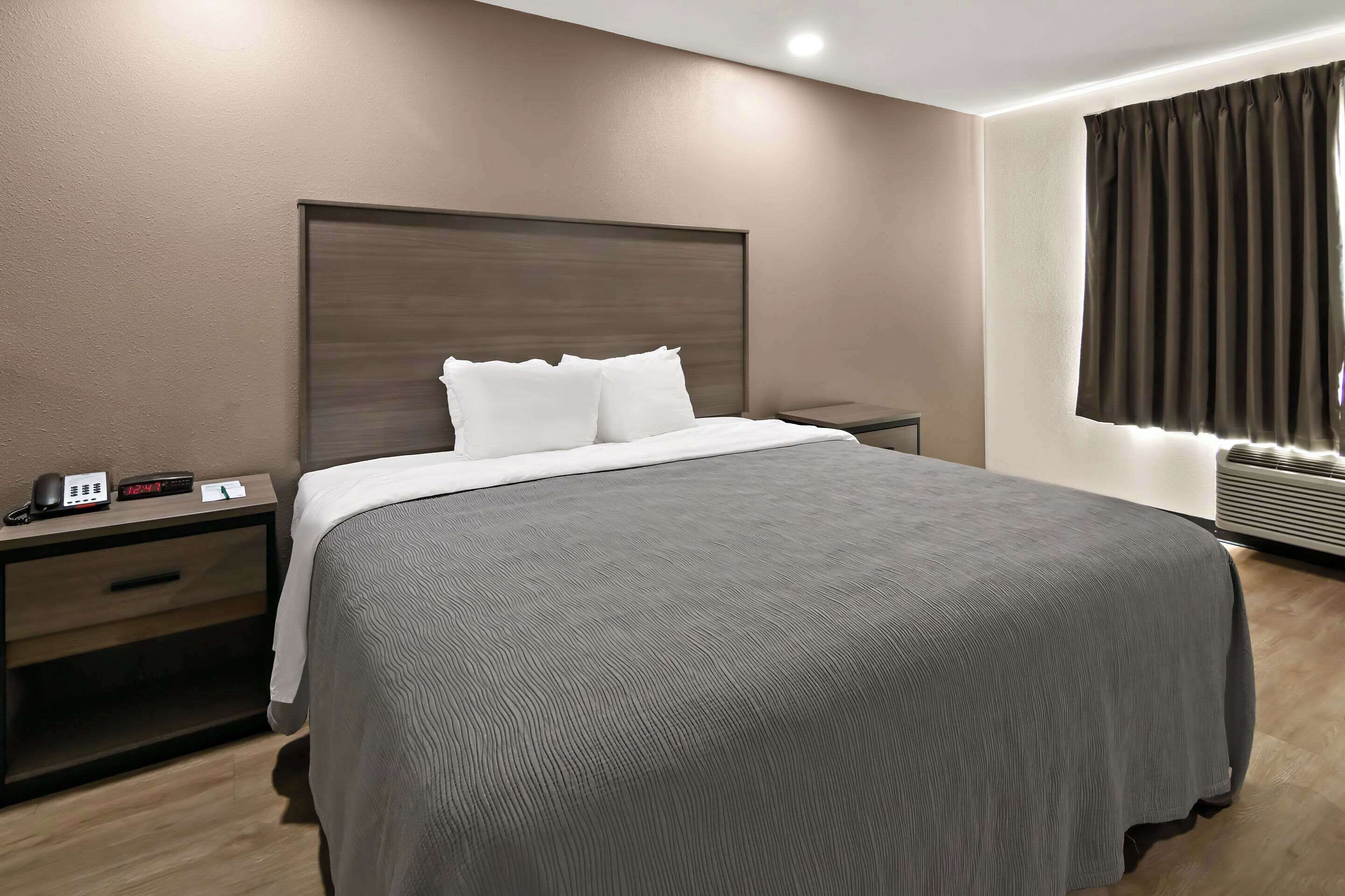 A hotel room with a large bed, a bedside table with a phone, a nightstand, and a window with curtains.