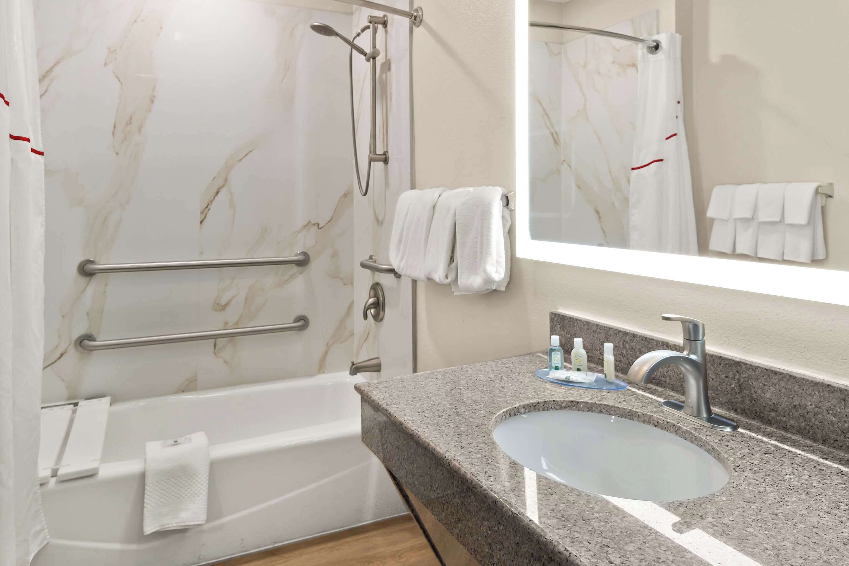 Un bagno con parete doccia in marmo, una vasca, un mobile lavabo e uno specchio.
