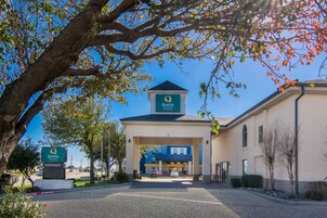 Entrada de un hotel con un cartel que dice 'Quality Inn & Suites' y un área de estacionamiento.