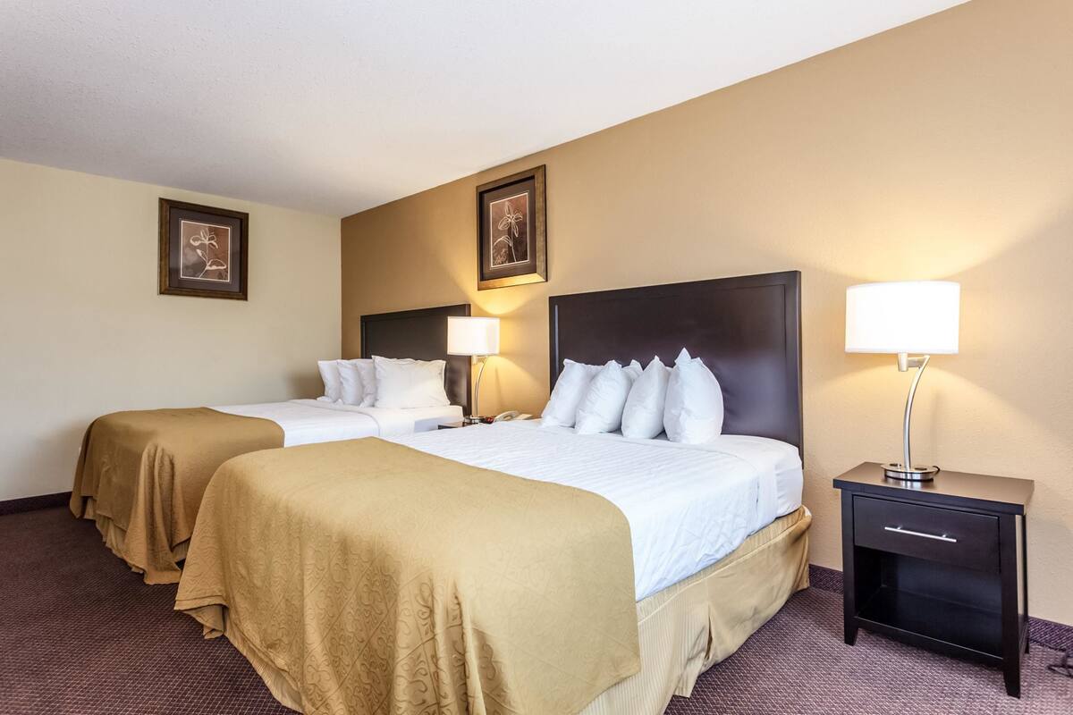 Habitación de hotel con dos camas, paredes color beige, cuadros enmarcados y lámparas de noche.