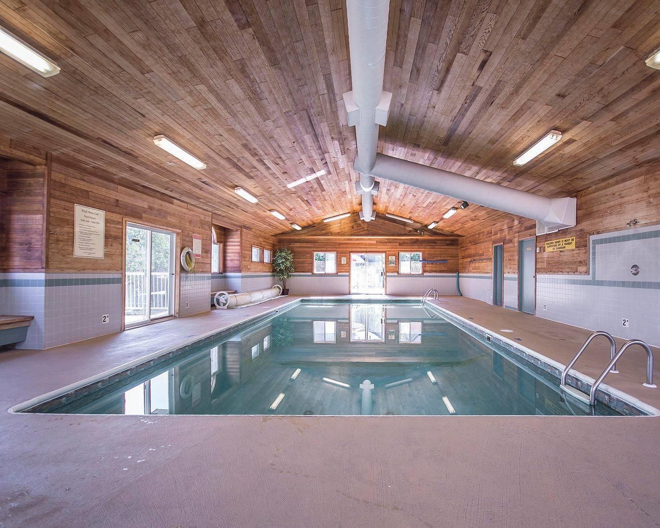 An indoor swimming pool with wooden walls and ceiling, clear signage, and a bench along the side.