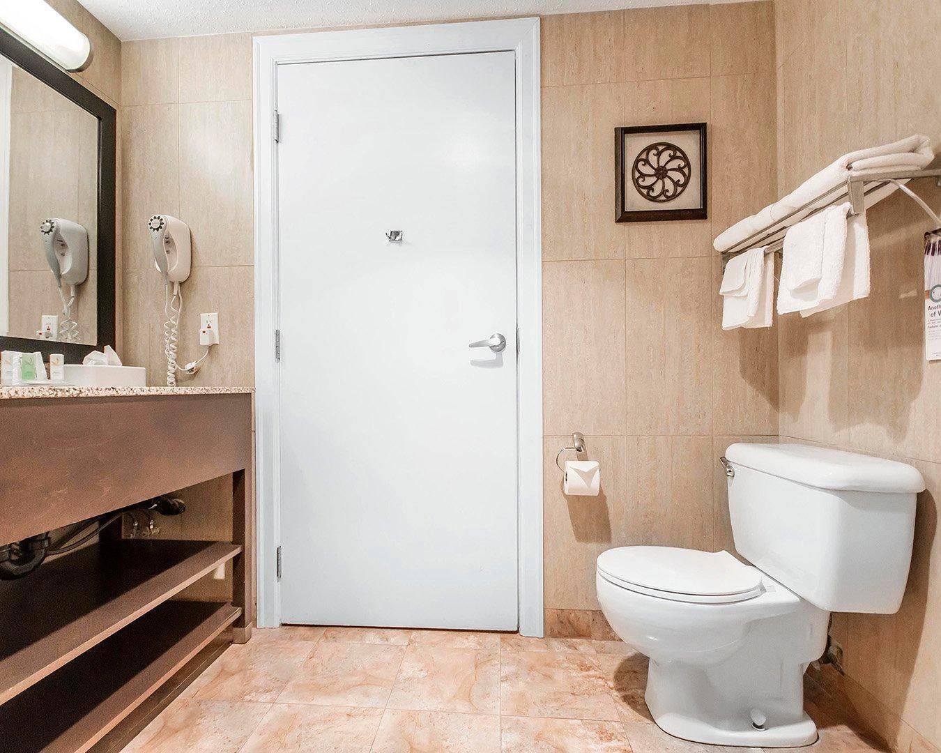 Un baño con inodoro blanco, un lavamanos con espejo y un perchero para toallas.