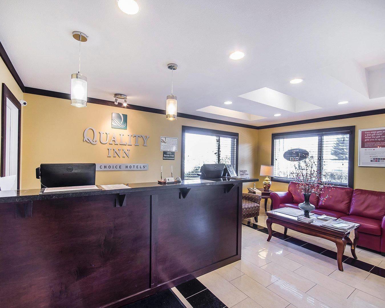 Un espace d’accueil avec un comptoir de réception sombre, une enseigne indiquant « Quality Inn » et un canapé rouge.