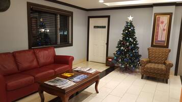 Un salón con un sofá de cuero rojo, una mesa de centro de madera con periódicos, un árbol de Navidad y un sillón estampado.