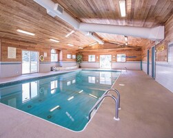 Una piscina interior con techo de madera, paredes de vidrio transparente y un banco a lo largo del borde.